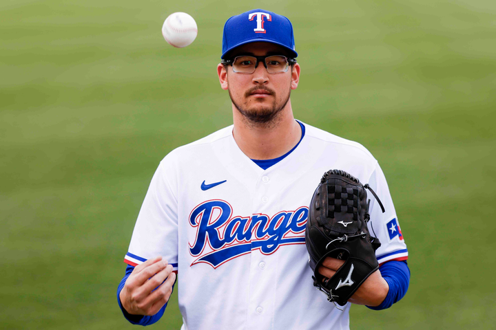 Dane Dunning in a Rangers uniform, tossing a ball into the air while looking at the camera